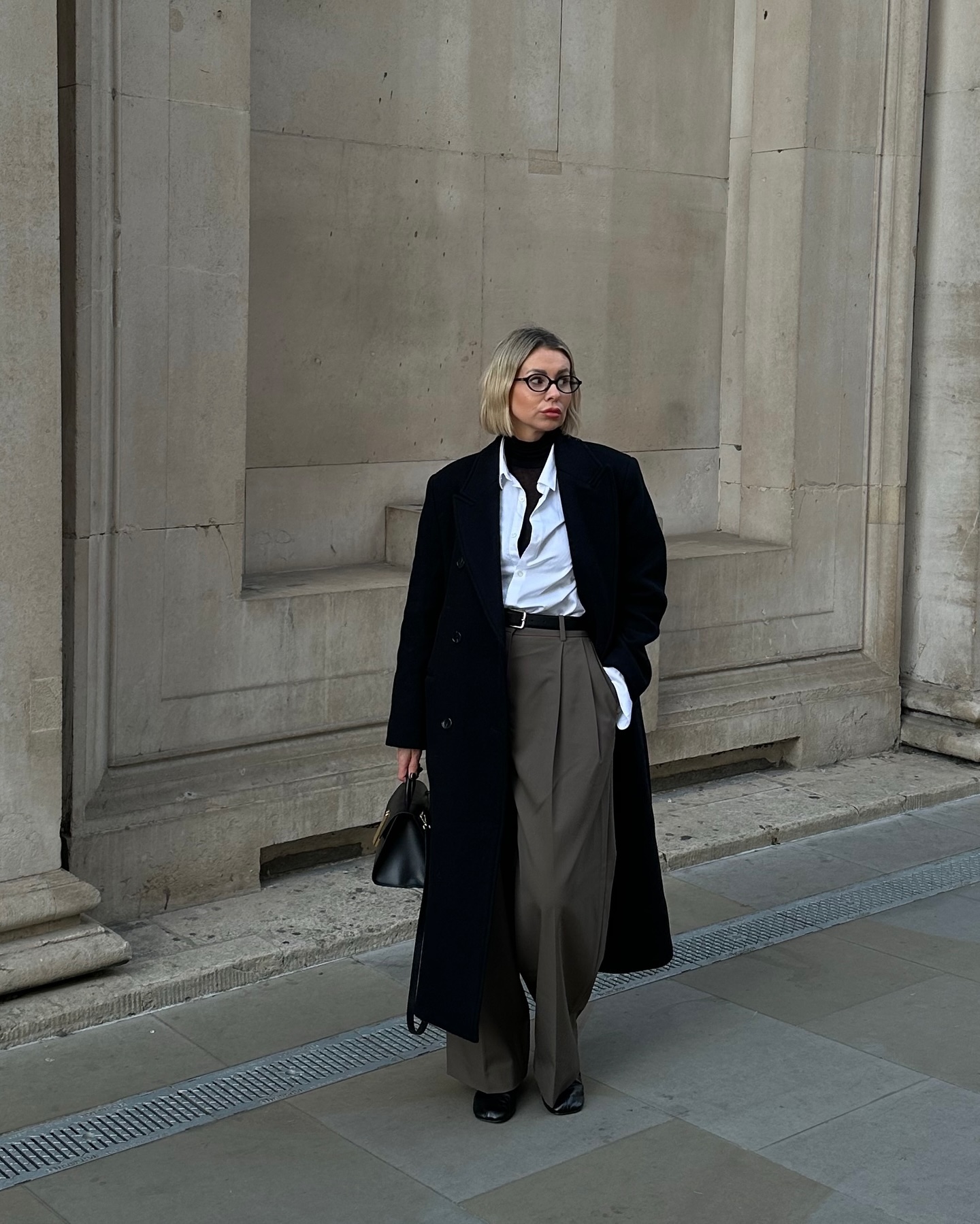 Office look featuring white shirt, black turtleneck, grey pants, black coats, black boots and bag