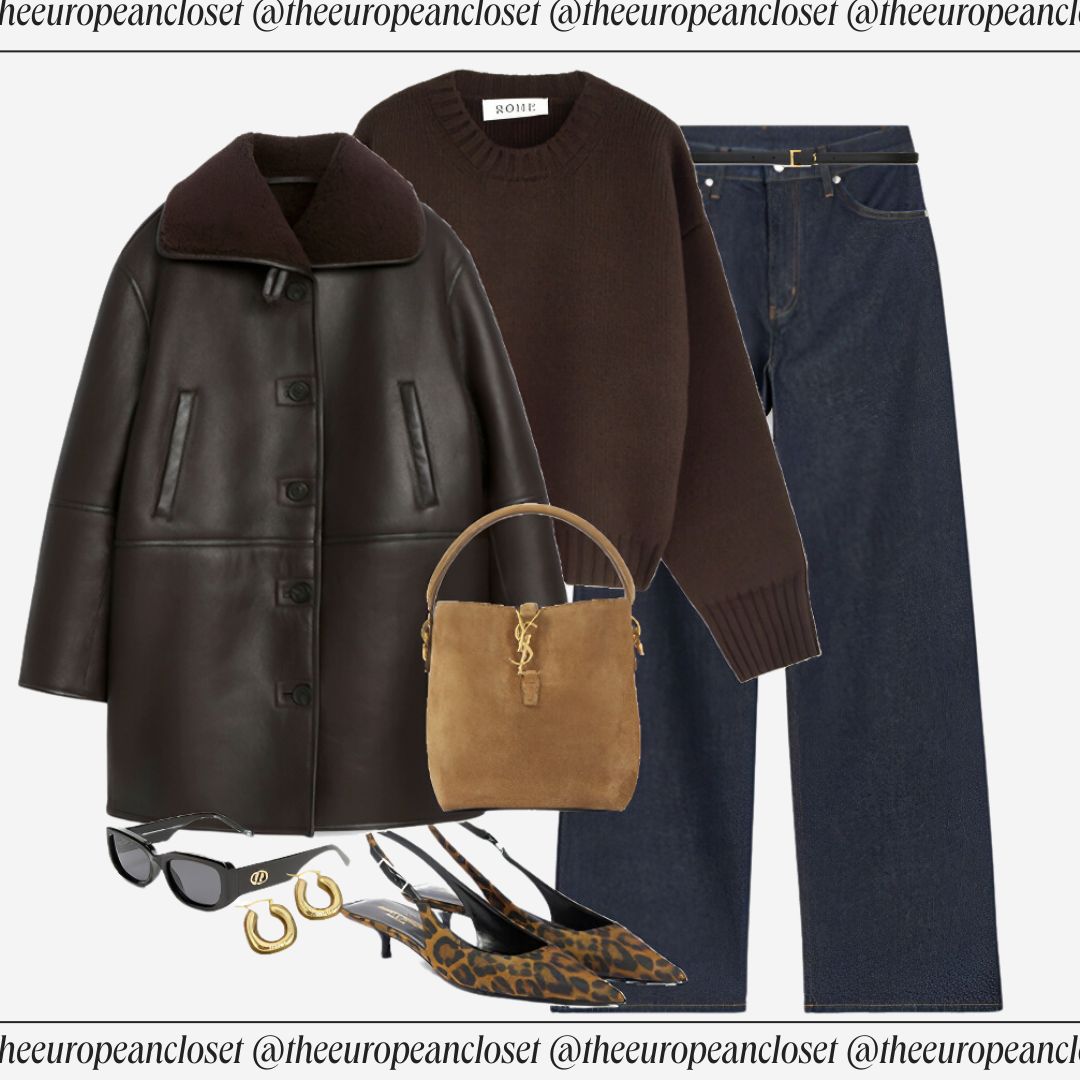 Flat lay of a brown leather jacket with a shearling collar and button closure, a brown crew neck sweater, and blue wide-leg jeans, accessorized with suede desert boots, a tan suede tote bag, dark tortoiseshell sunglasses, and a brown braided belt.